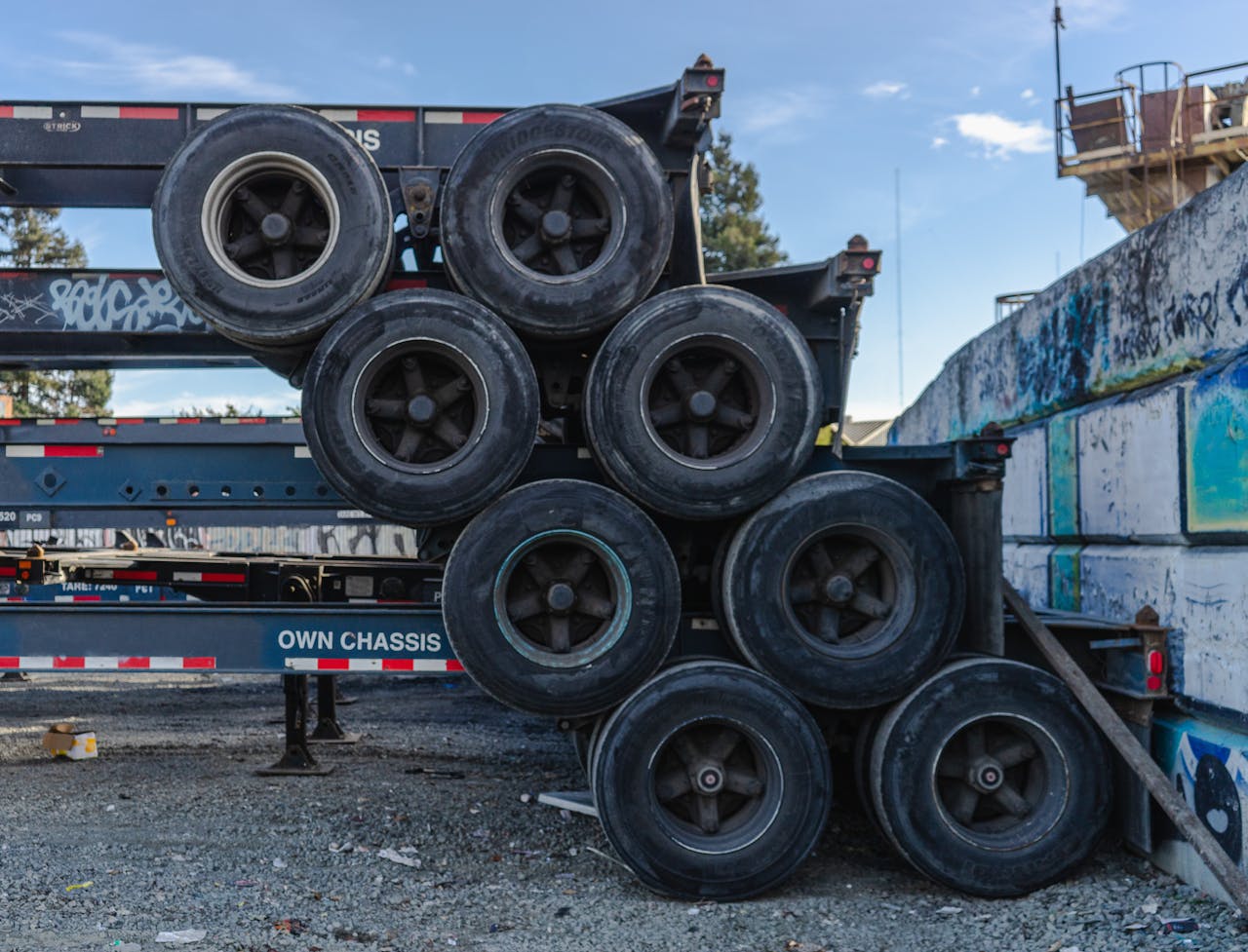 Row of stacked truck tires on chassis in an industrial area.